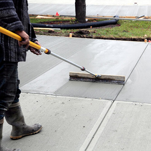Concrete worker trowels a freshly poured sidewalk.